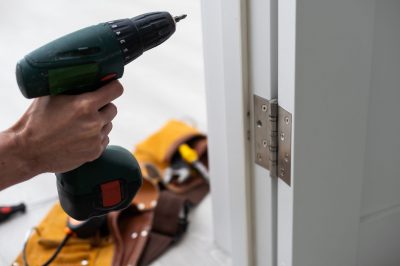 A powered screwdriver next to the finished hinges of a door replacement.