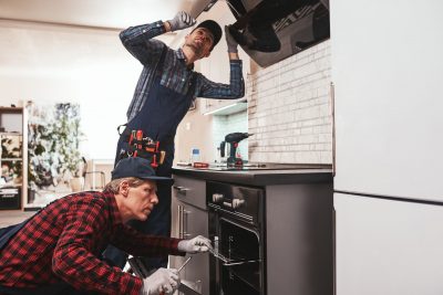 Two handymen installing a stove and vent hood appliance. Two handymen installing a stove and vent hood appliance.